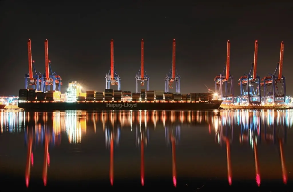 Container cranes lit up at night, reflected in the water